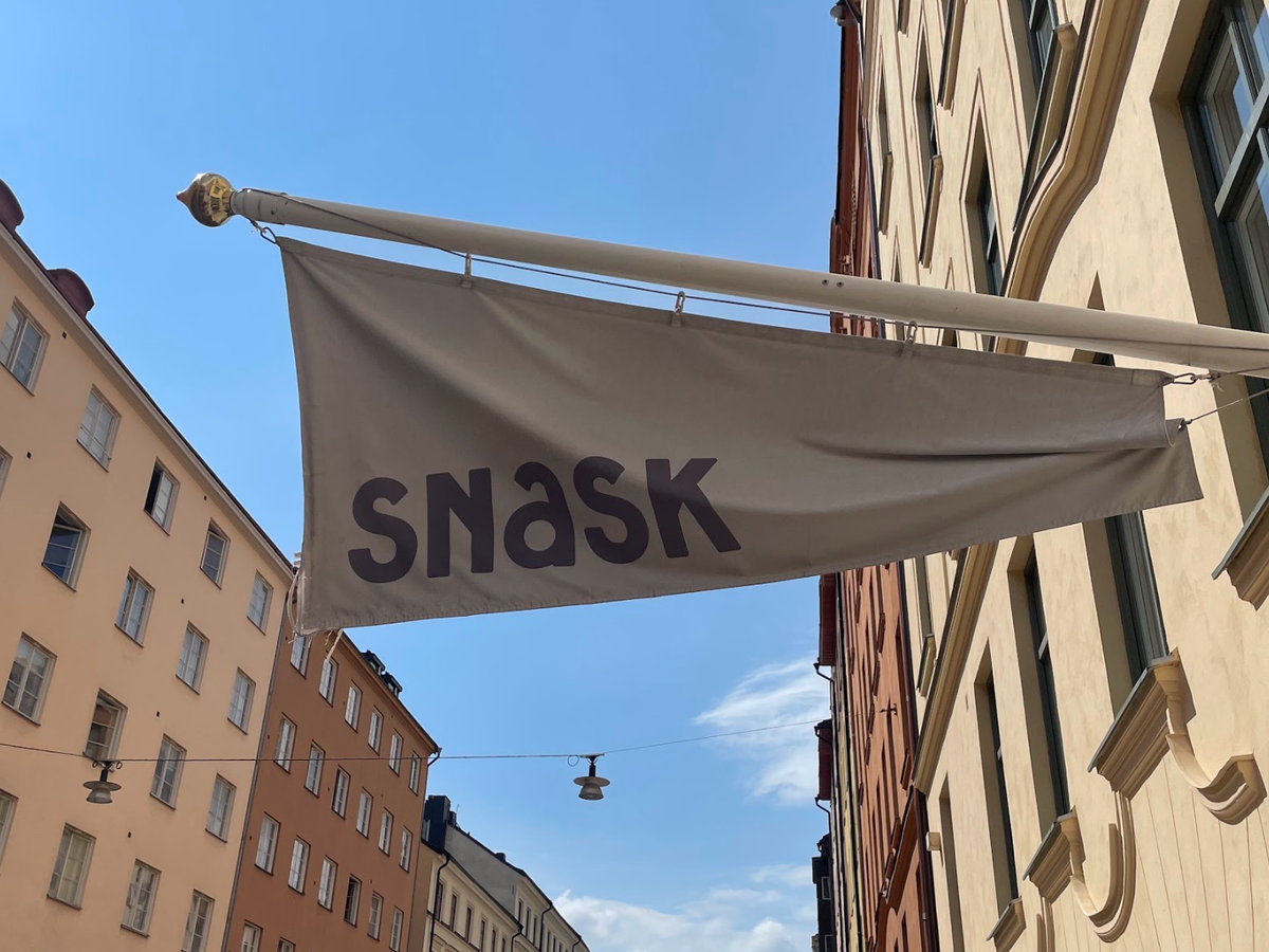 White flag that reads "Snask" above a tan building.