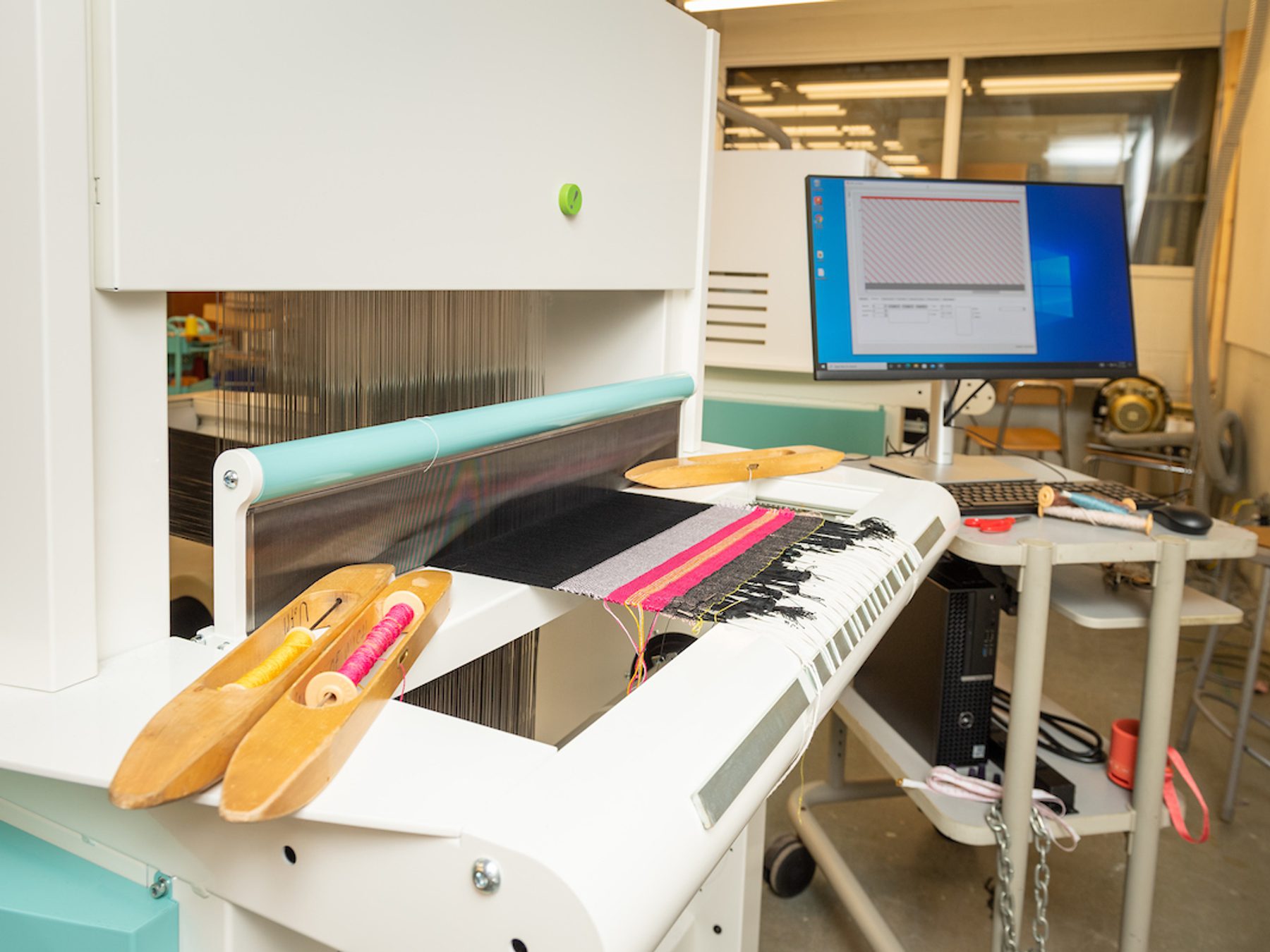 Digital loom and computer. Colorful threads rest on the loom.