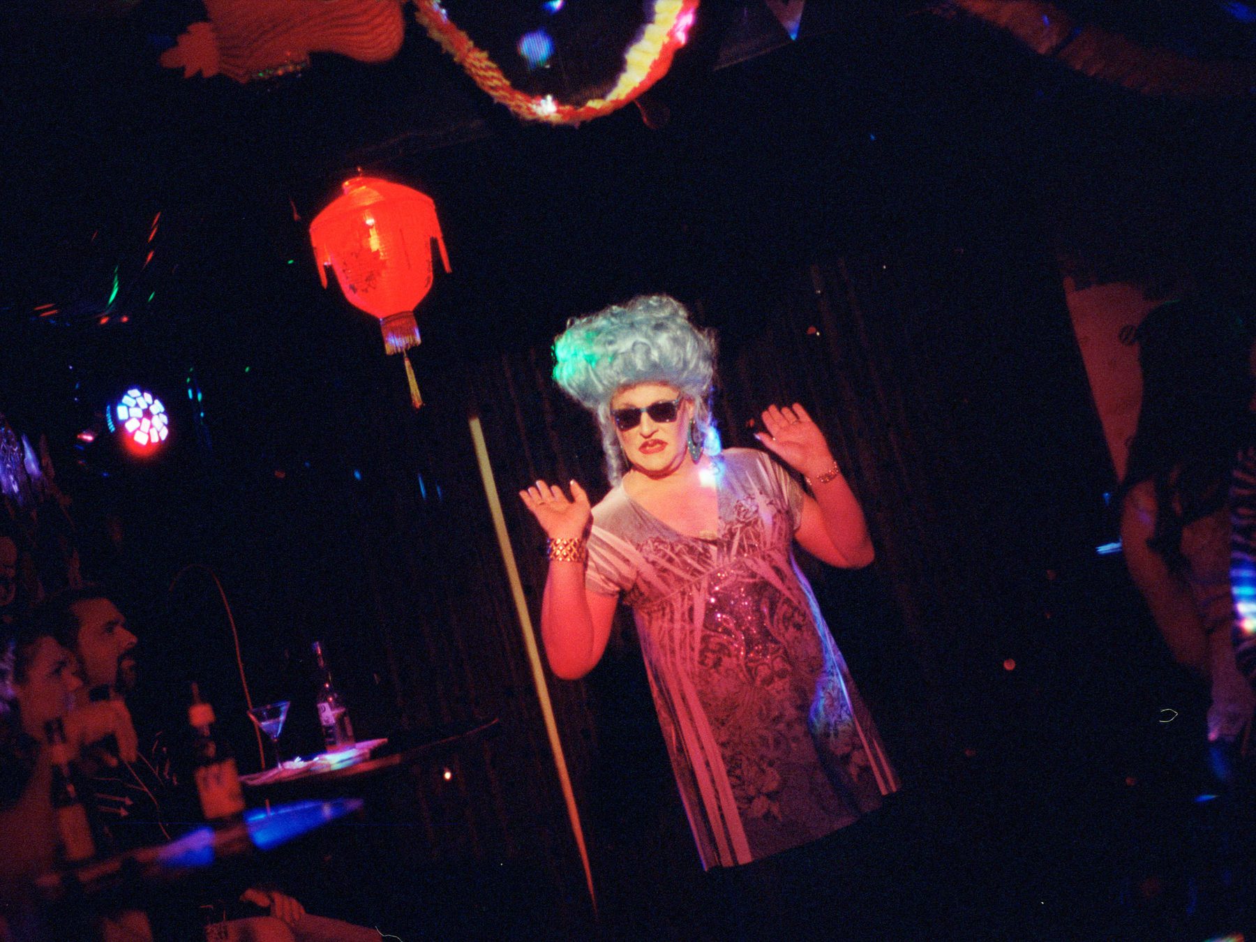 A drag queen in sunglasses dancing in a nightclub.