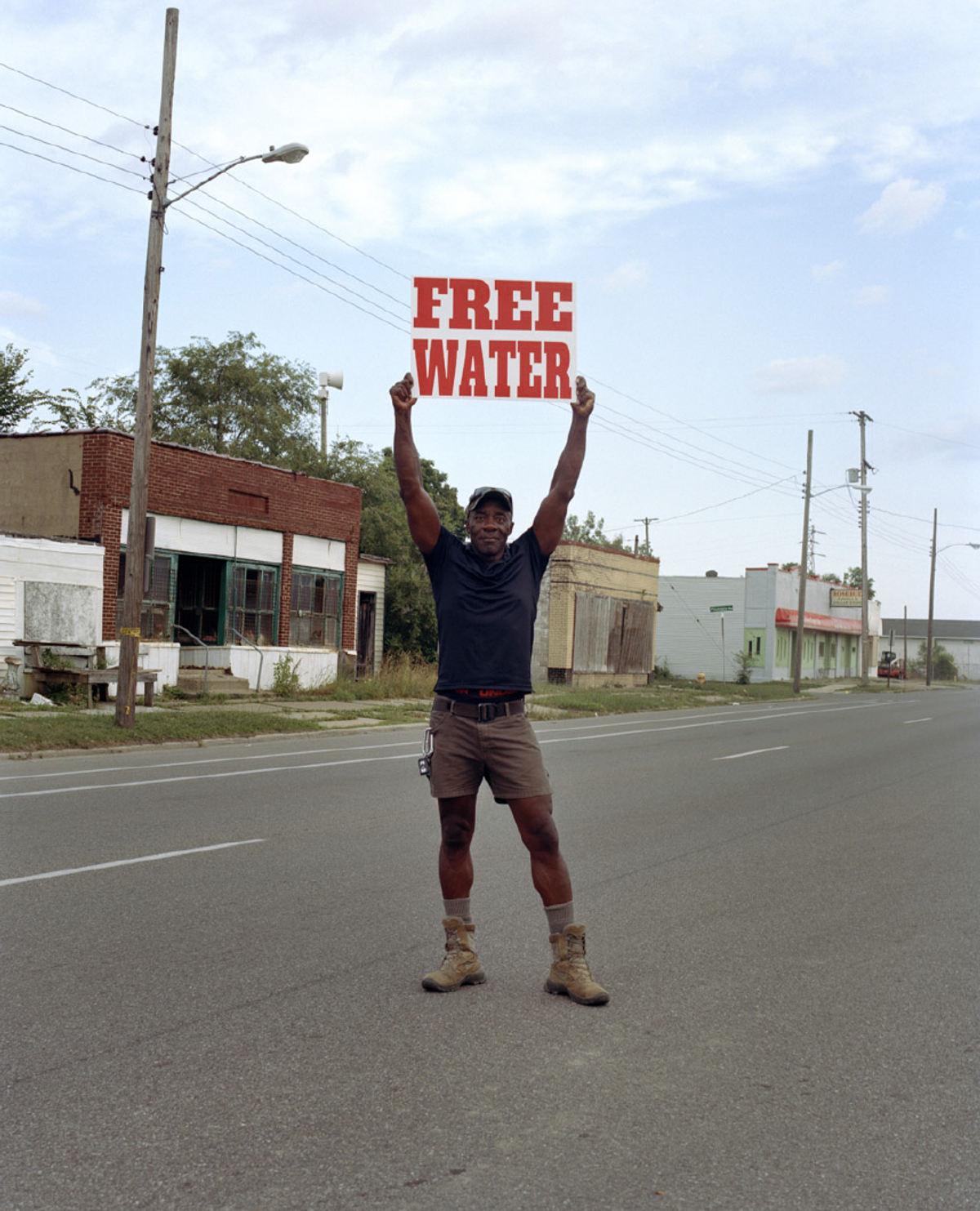 LaToya Ruby Frazier, "Moses West Holding a “Free Water” Sign on North Saginaw Street Between East Marengo Avenue and East Pulaski Avenue, Flint, Michigan", 2019/2020.