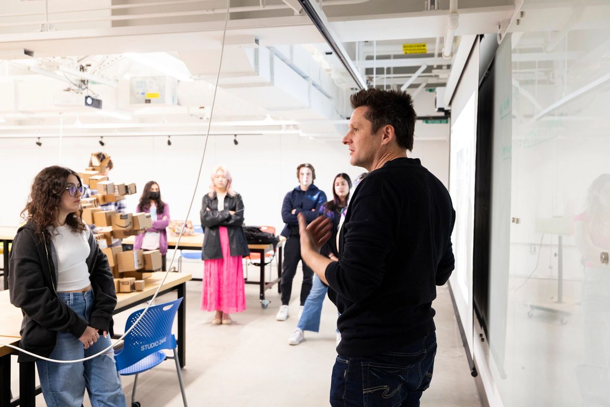 Instructor stands at a white board in a well lit classroom