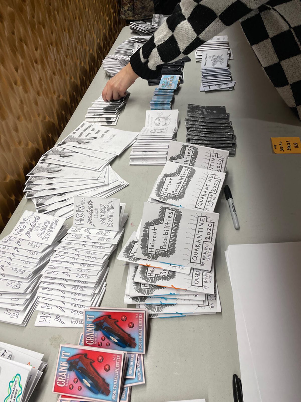 A table features several stacks of handmade zines, along with sharpie markers and paper