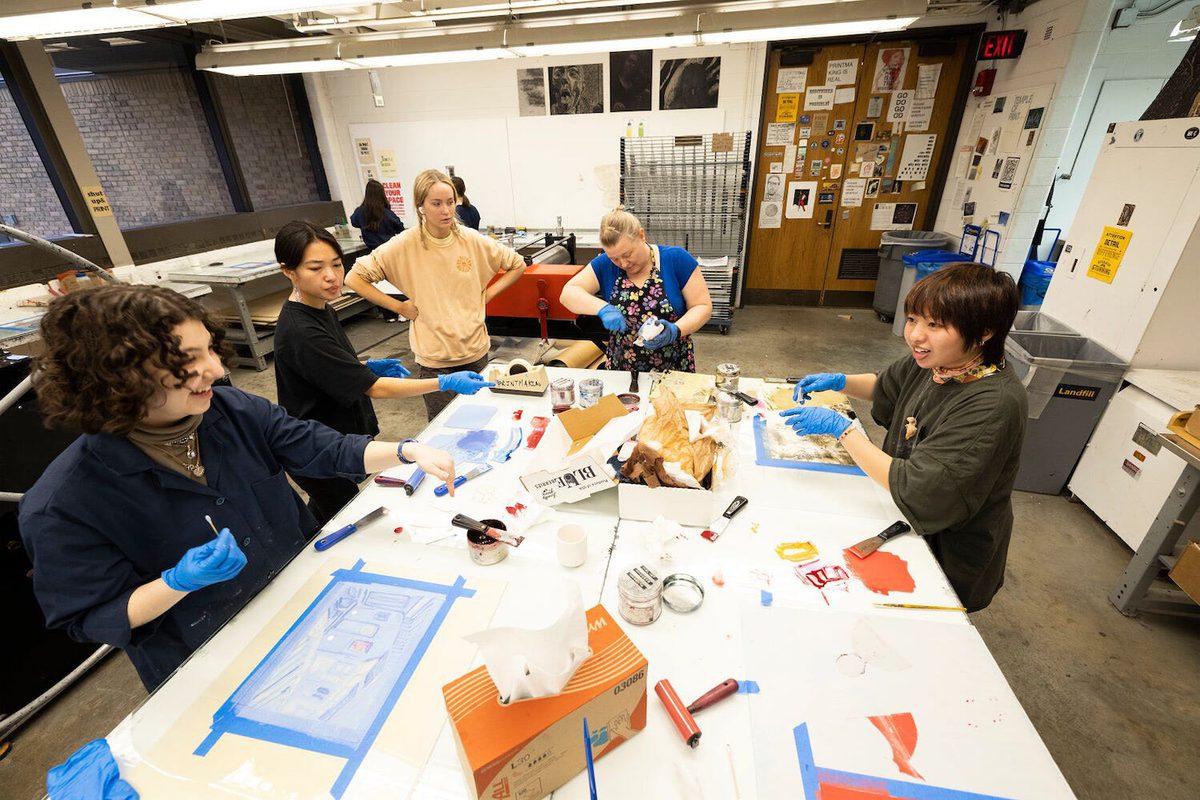 Students and faculty collaborate around a table in the printmaking studio.