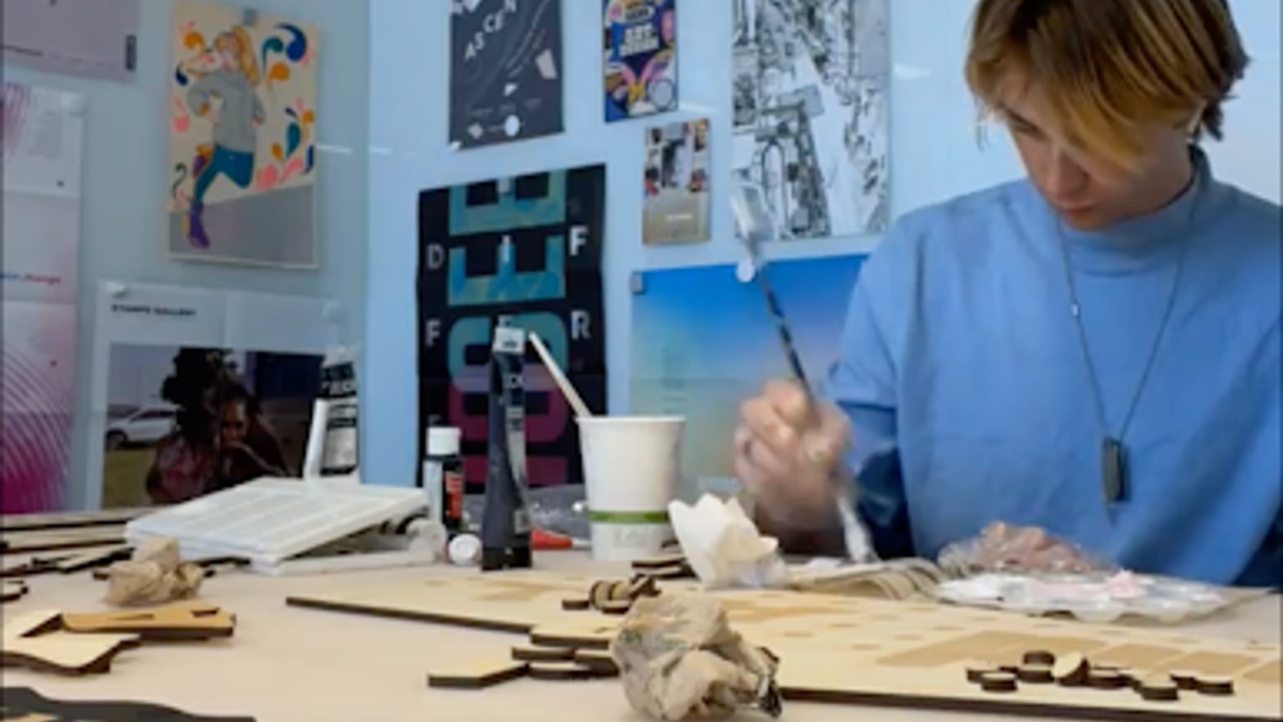 Jake Schraga sits at a table with wood letters while applying wood glue using a paintbrush.